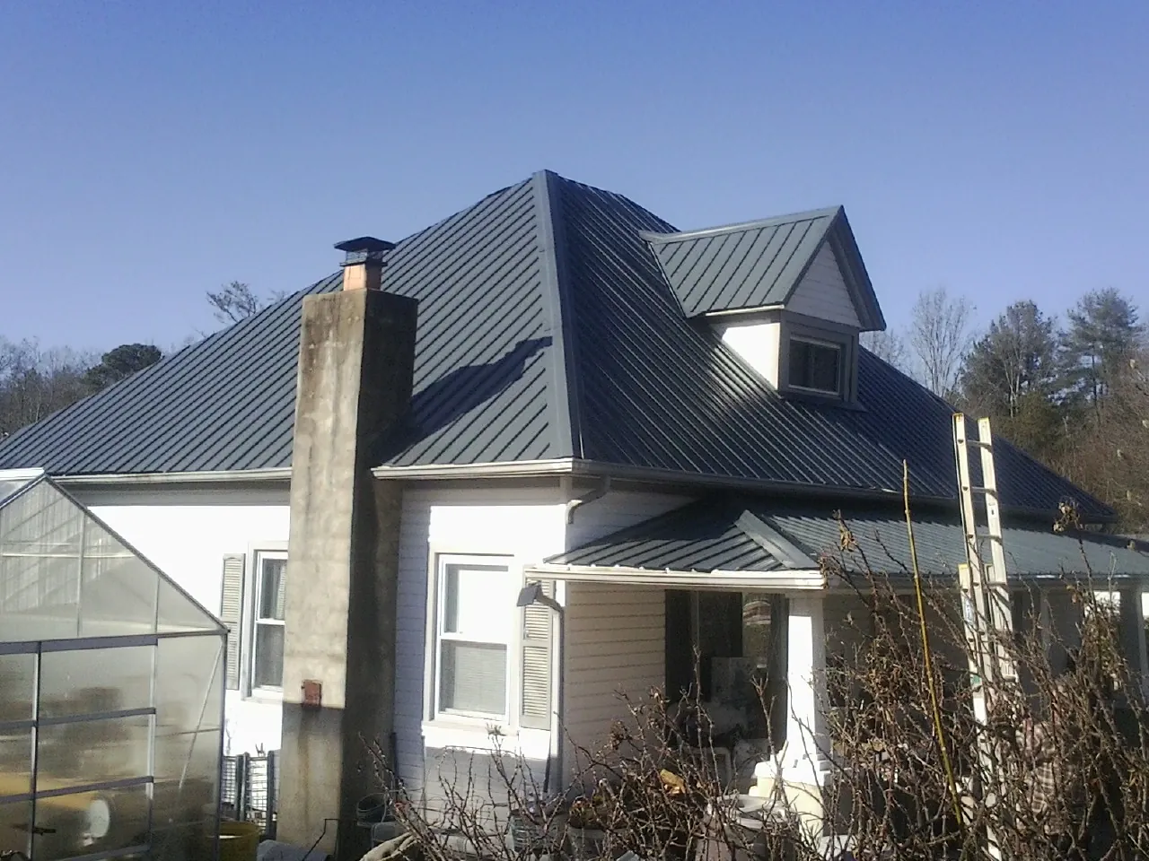 Dark blue standing seam metal roof on a white farmhouse with dormer — Slate & Tile Roof Repair by Roofing Brothers in Gorham