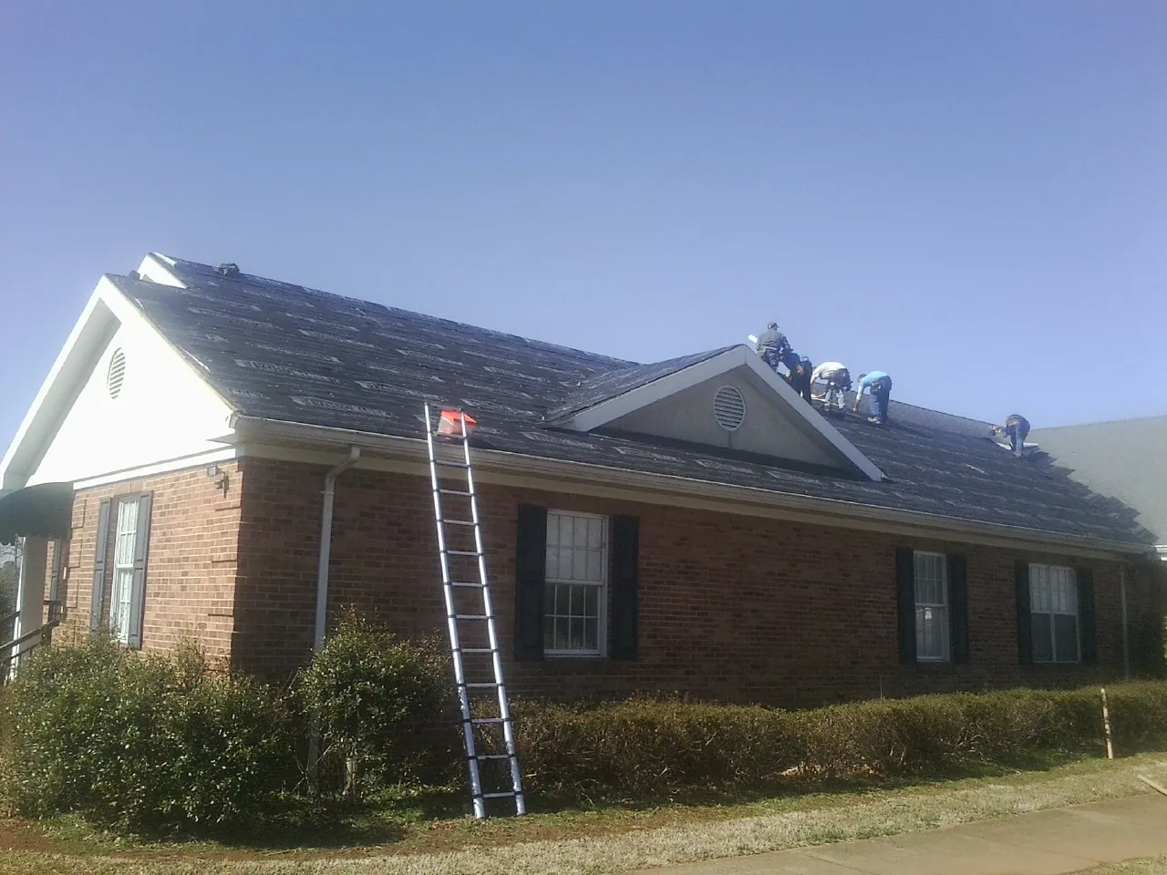 Crew tearing shingles off a brick ranch roof with a ladder set — Metal Roof Repair work by our crew in Gorham