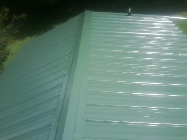 New green metal panels meeting at the ridge of a roof — Flat Roof Repair work by our crew in Gorham